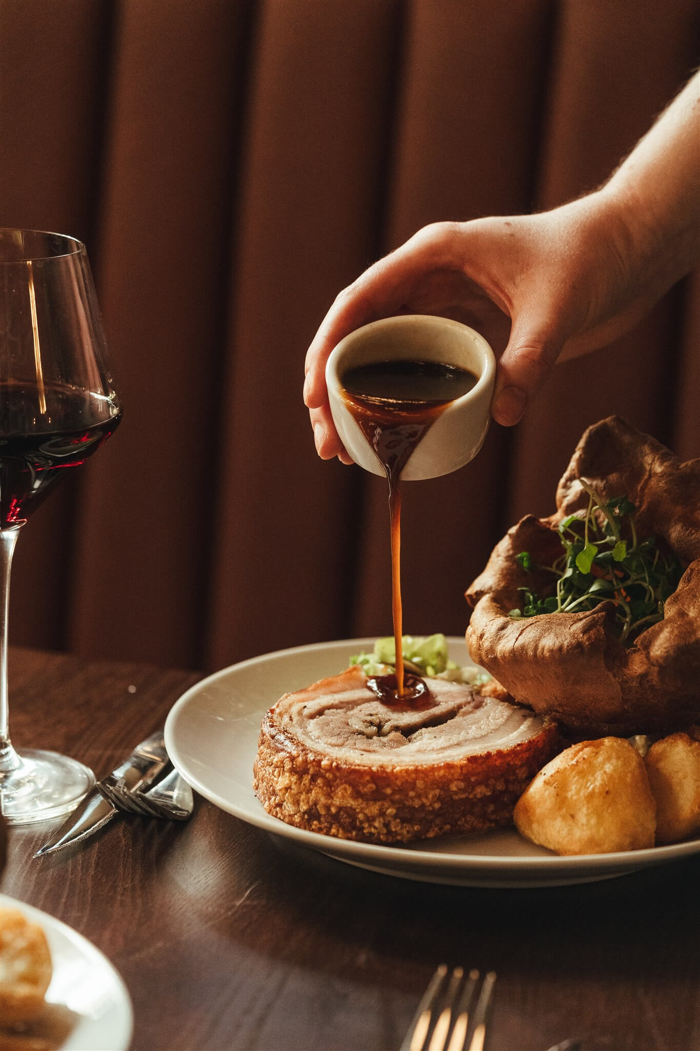 Gravy poured over pork belly with a Yorkshire pudding and red wine