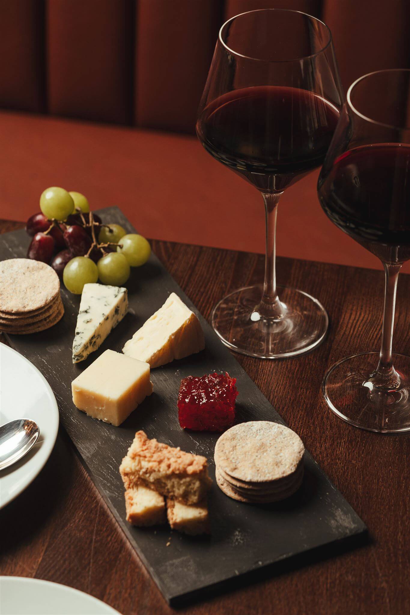 Two glasses of red wine with a board of cheese and accompaniments